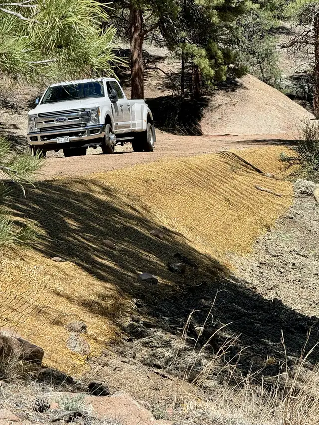 Erosion control blanket freshly installed on a slope beside a graded mountain road with a white Ford Super Duty truck in the background in Conifer, Colorado
